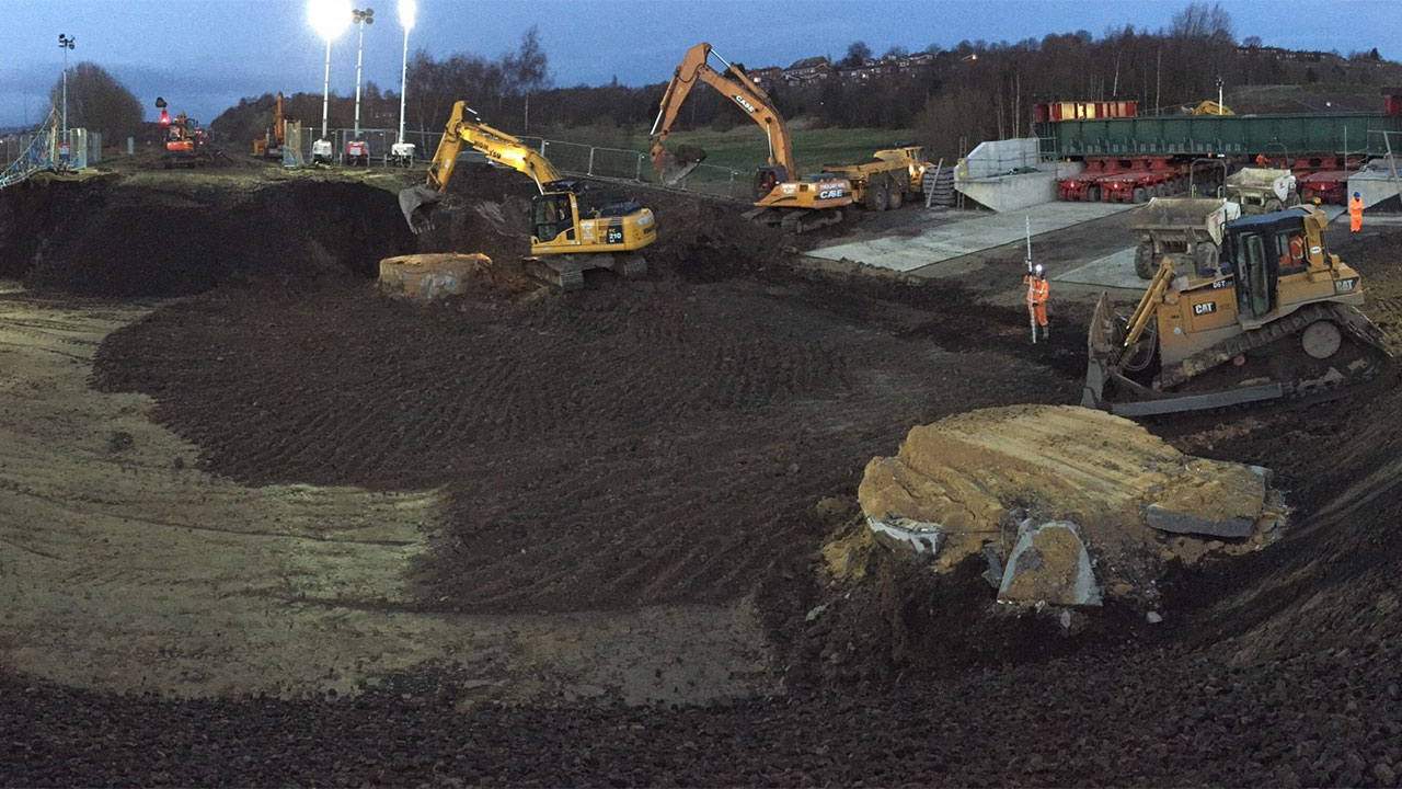 Construction equipment digging up dirt at a worksite, with machinery actively moving soil and debris