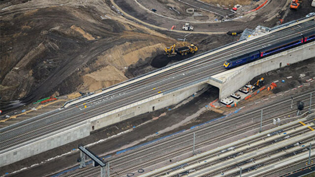 A train travels on a bridge, overlooking a busy construction site below