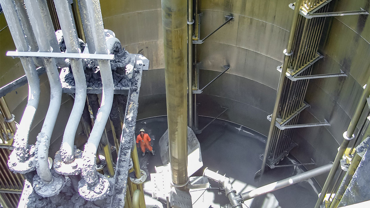 A worker stands inside a large metal tank, wearing safety gear and inspecting the interior structure
