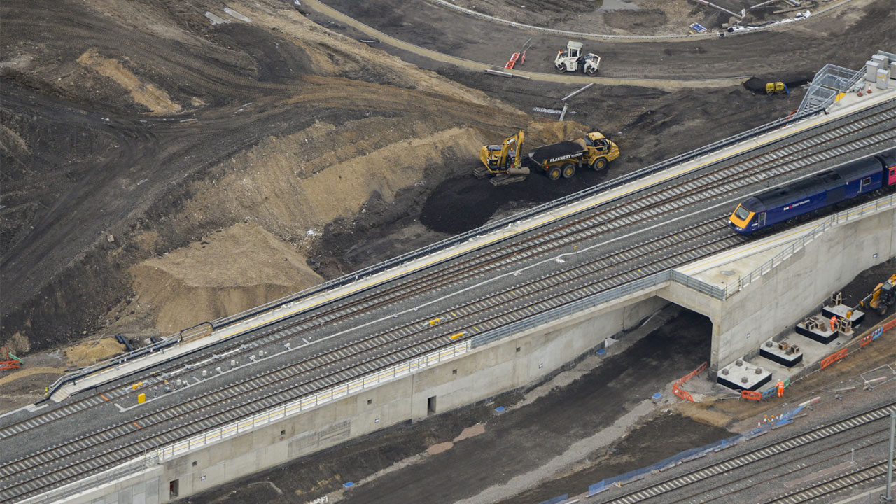A train travels on a bridge, overlooking a busy construction site below